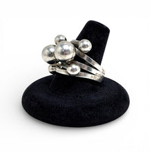 Silver ring with spherical designs on a black stand against a white background